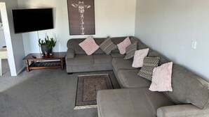 Un salon avec un canapé gris, un téléviseur à écran plat, une table basse et un tapis à motifs.