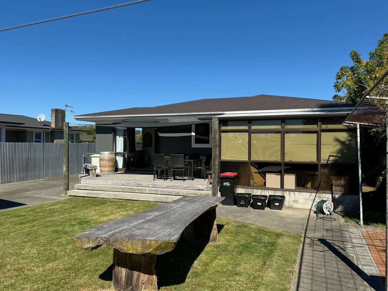 A covered outdoor area with a picnic table, chairs, and a barbecue grill.