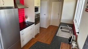 Une cuisine compacte équipée d’un réfrigérateur en acier inoxydable, d’un four à micro-ondes et d’une cuisinière. On y trouve un plan de travail en bois et un évier avec un robinet. Le sol est en bois et un petit tapis est posé dans un coin.