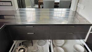 Eine Küche mit Glasarbeitsplatte, einer integrierten Schublade für Besteck und einem Essbereich im Hintergrund.