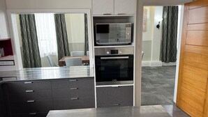 Eine moderne Küche mit integriertem Mikrowellenherd, Backofen und Spüle. Durch eine offene Tür ist ein Essbereich mit Tisch und Stühlen zu sehen.