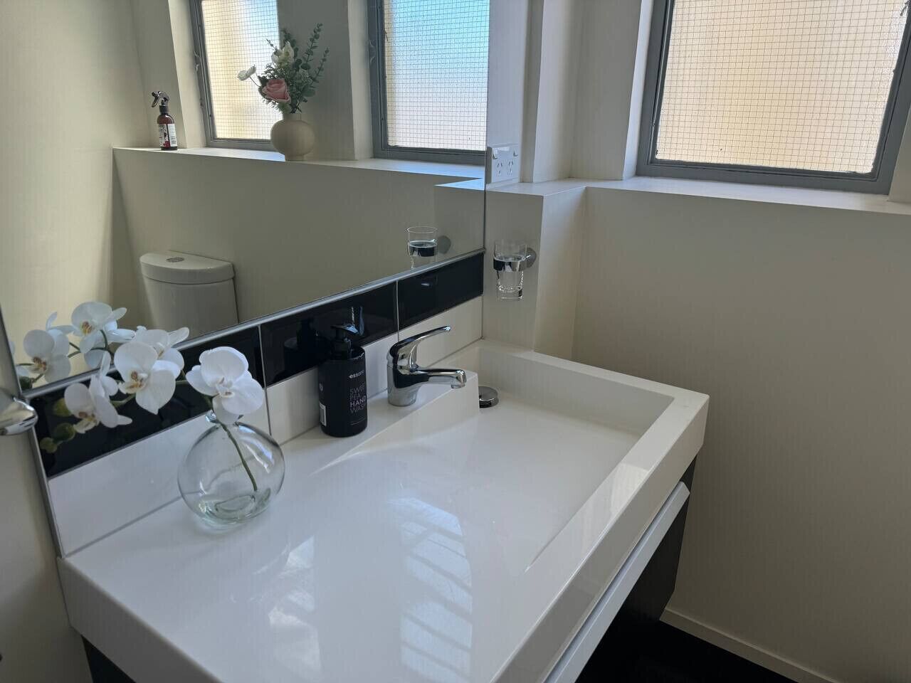 A modern bathroom with a white sink, a large mirror, and a window.