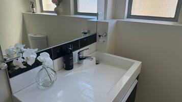 A modern bathroom with a white sink, a large mirror, and a window.