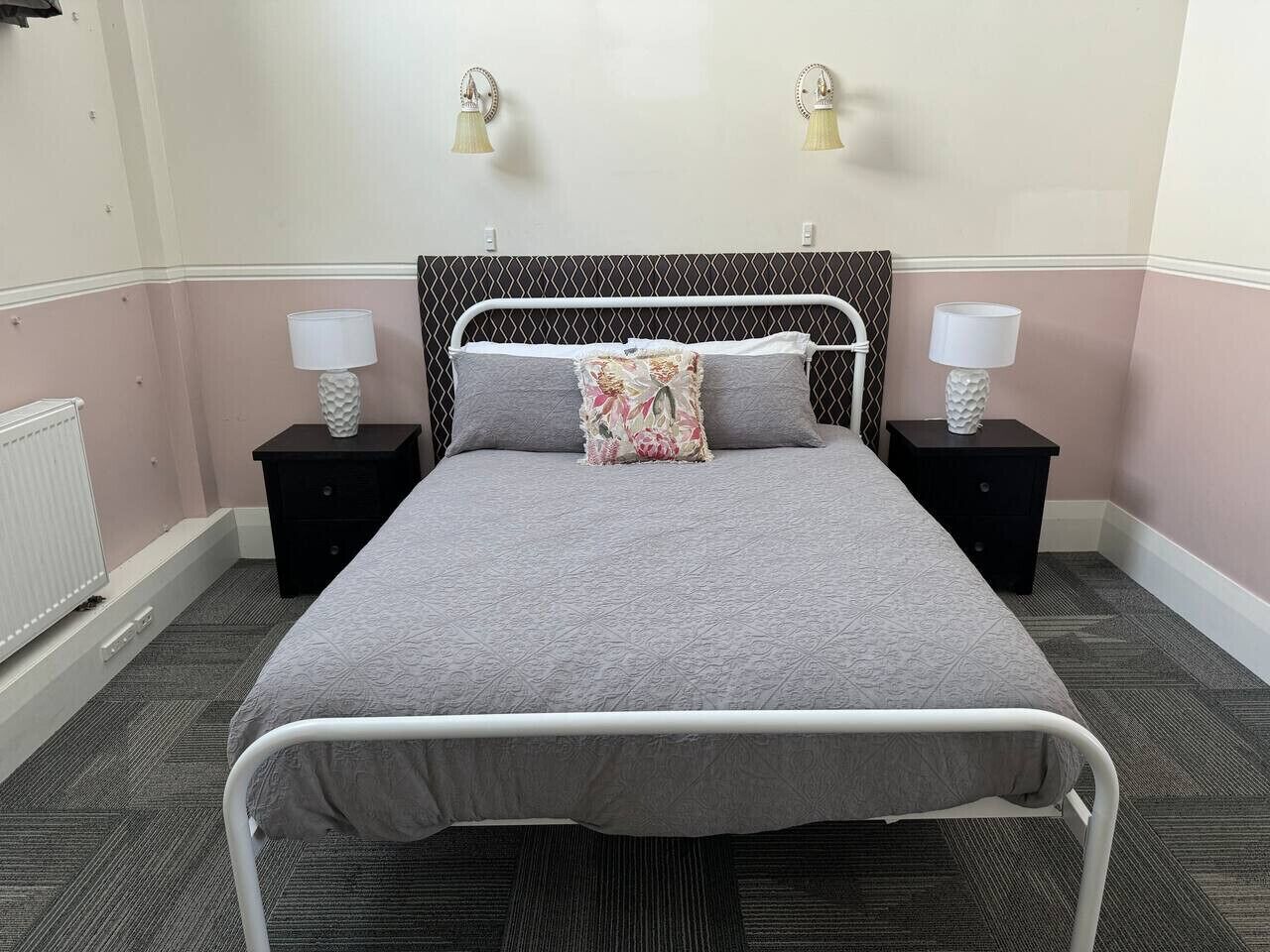 A neatly made bed with a grey bedspread, two bedside tables with lamps, and a decorative pillow.