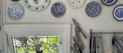 A kitchen with various plates hanging on the wall, a window with a view, and kitchen utensils hanging on the wall.