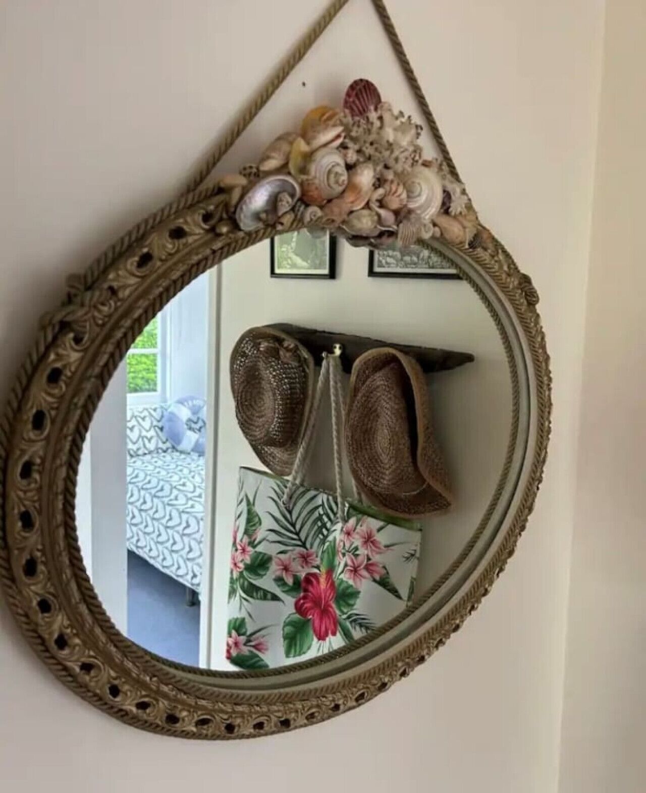 A mirror with an ornate frame, a pair of brown woven bags, and a floral-patterned pillow on a bed.