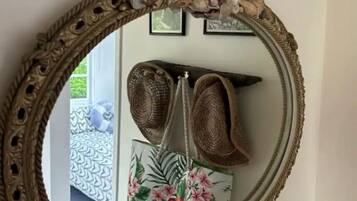 A mirror with an ornate frame, a pair of brown woven bags, and a floral-patterned pillow on a bed.