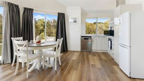 A modern kitchen with white appliances, a dining area with white chairs, and large windows with curtains.