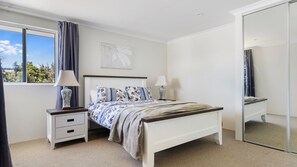 A bedroom with a bed, two bedside tables, a window with curtains, a wall-mounted artwork, and a mirror. - Hill View Cottages – Sail A & Sail B in Picturesque Nannup (Nannup)