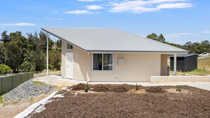 A modern single-story house with a flat roof, a small porch, and a well-maintained garden with mulch and young plants. - Hill View Cottages – Sail A & Sail B in Picturesque Nannup (Nannup)