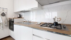Una cocina moderna con armarios blancos, salpicadero de mármol, estufa a gas, hervidor y cafetera.