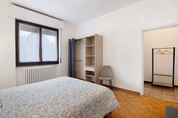 A bedroom with a bed, a wardrobe, a radiator, and a window with curtains.