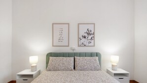 Un dormitorio con una cama, dos mesitas de noche, un cabecero tapizado en verde y dos cuadros enmarcados en la pared.