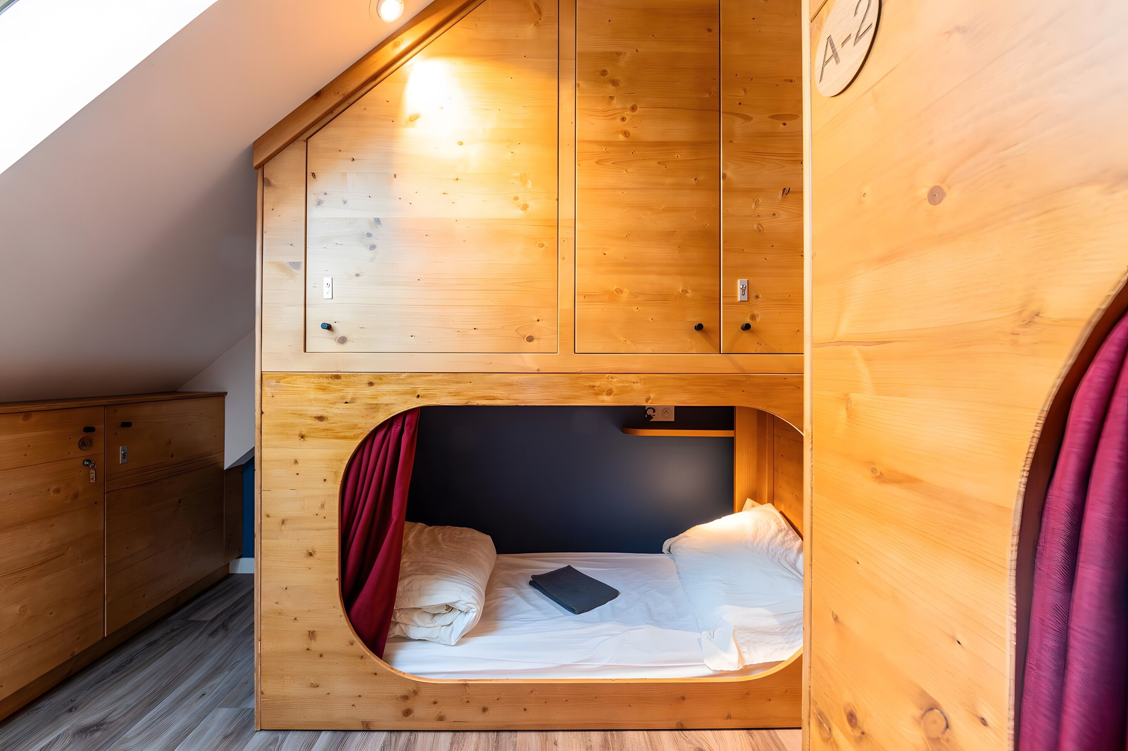 Een houten stapelbed met een rood gordijn, een zwart boek en een wit kussen.