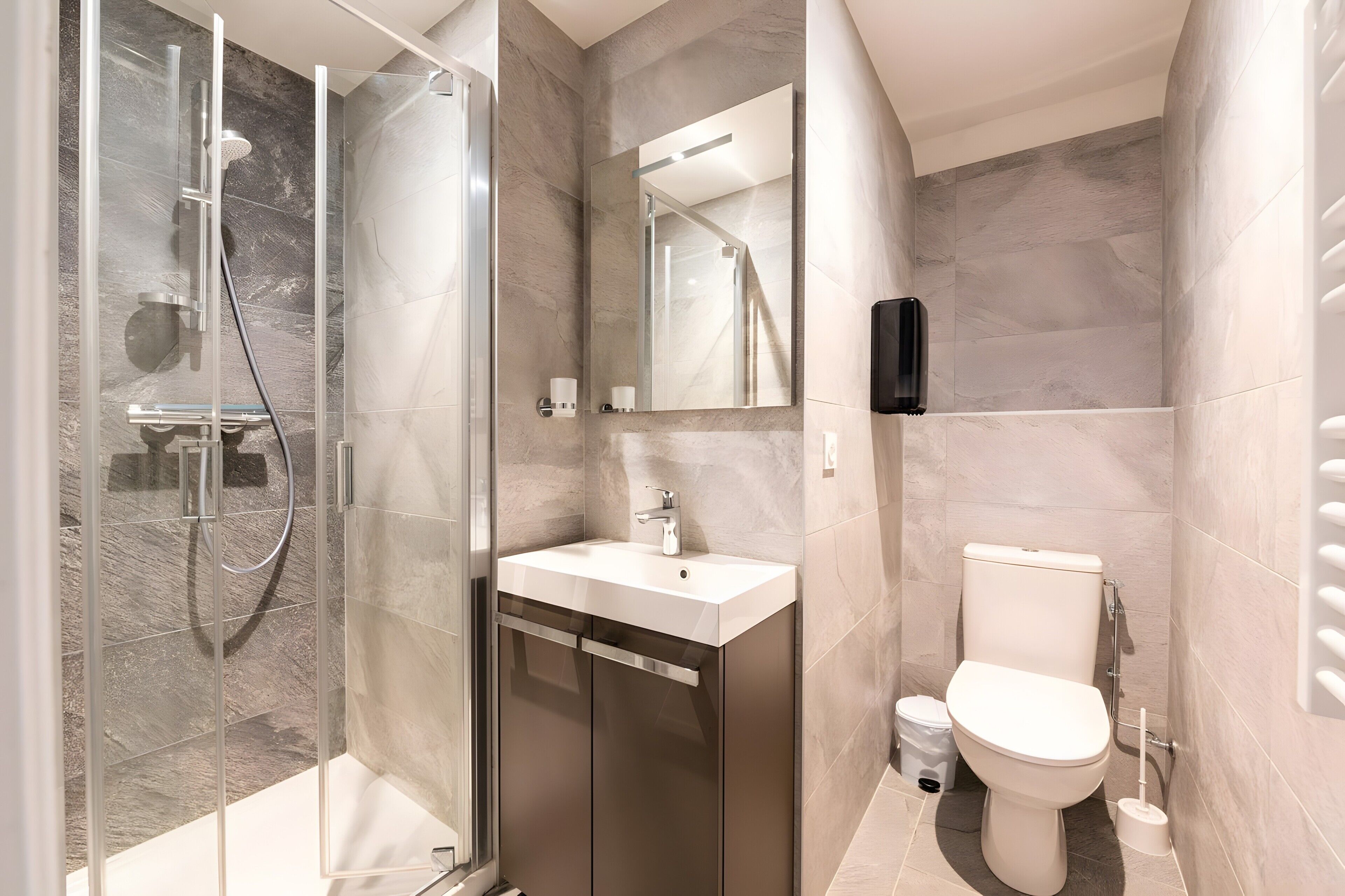 Ein modernes Badezimmer mit Duschkabine, Waschbecken, Toilette und Spiegel.