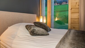 A bed with two pillows, a bedside lamp, and a view of houses through a window.