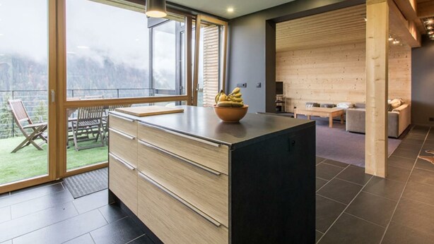 A modern kitchen with large windows, a dining area, and a living space with a view of the outdoors.
