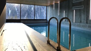 An indoor swimming pool with a view of snowy trees through large windows.