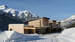 A modern wooden cabin with a flat roof, situated in a snowy mountainous area.