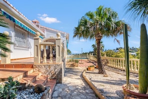 A courtyard with a palm tree, a cactus, and a white building with a balcony.