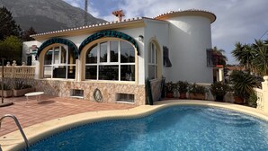 Et hus med swimmingpool, et bjerg i baggrunden og en klar himmel.