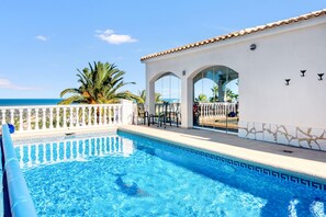 A swimming pool with clear blue water, a white building with arches, and a view of the ocean.
