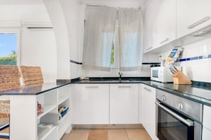Una cocina compacta con armarios blancos, una encimera negra, un microondas, un horno y una ventana con cortinas.