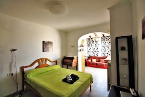 Um quarto com cama, escrivaninha, cadeira, sofá vermelho e espelho.