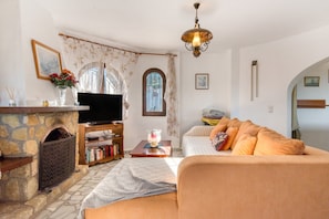 Ein Wohnzimmer mit Kamin aus Stein, einem Fernseher, einer Couch und einem Bücherregal.