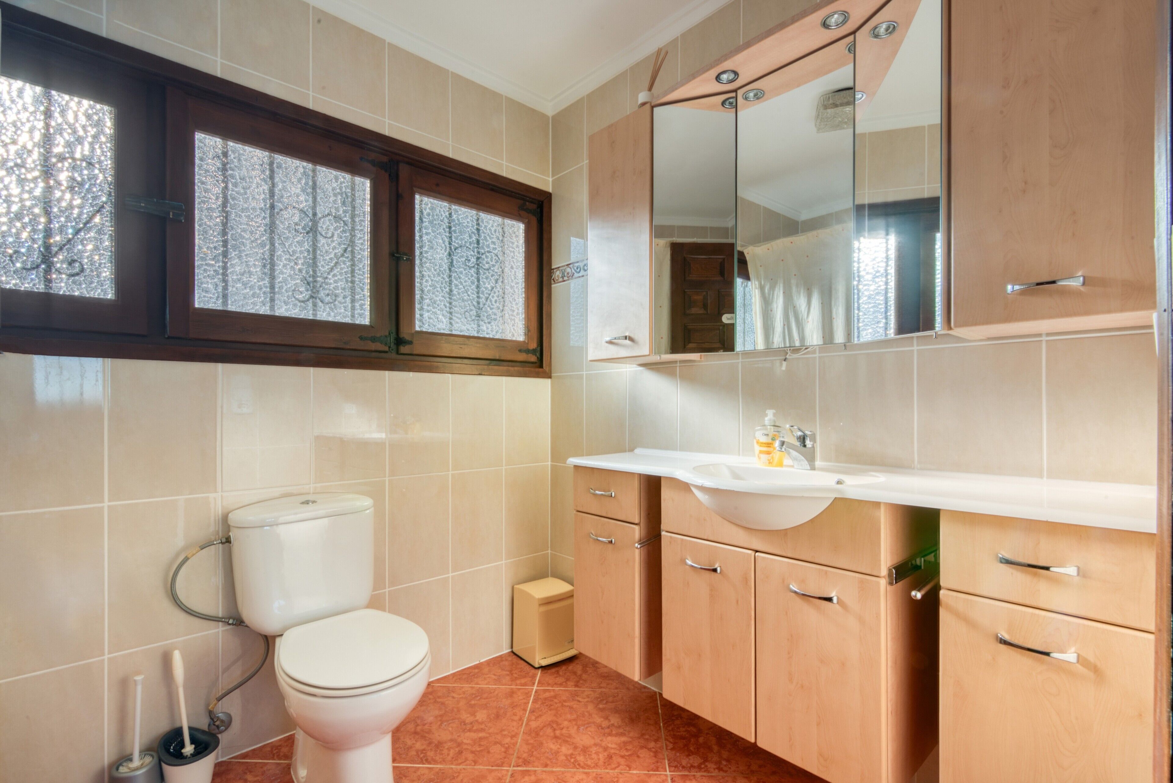 A bathroom with a toilet, sink, cabinet, mirror, and window.
