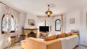 Una sala de estar con sofá, televisor, chimenea y suelo de piedra.