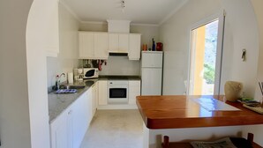 Ett kompakt kök med vita skåp, en mikrovågsugn, en ugn och ett matbord i trä.