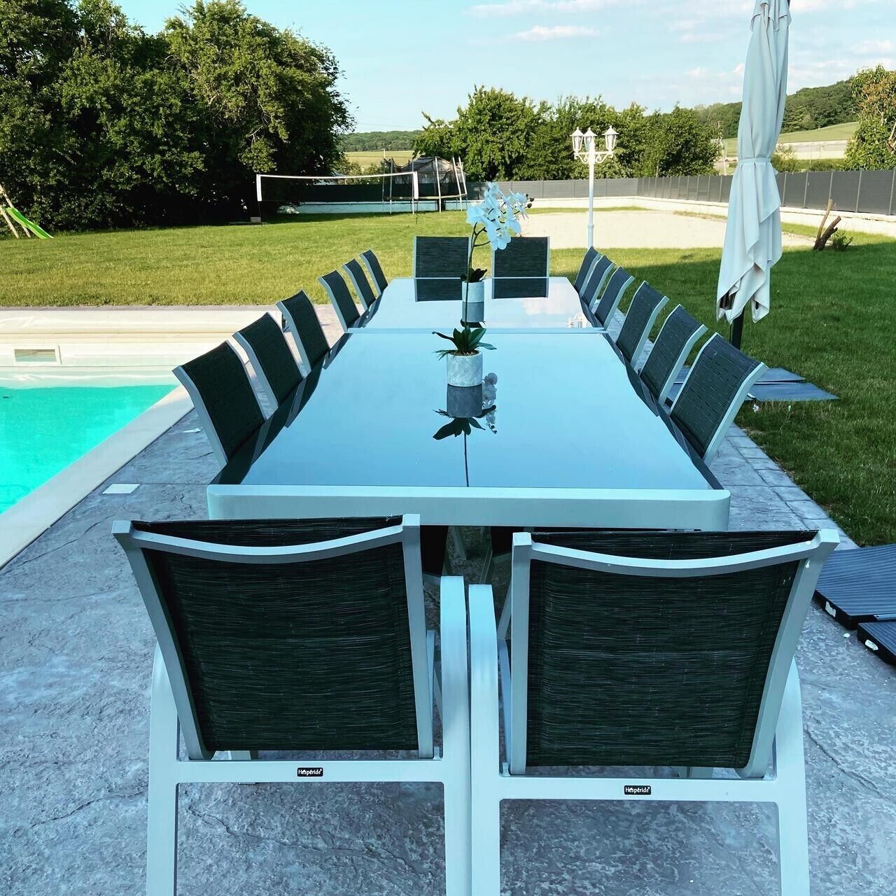 Una mesa rectangular para comer al aire libre con sillas, una planta pequeña en maceta y una piscina al fondo.