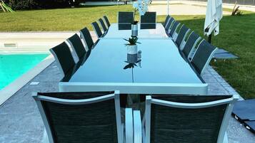 Una mesa rectangular para comer al aire libre con sillas, una planta pequeña en maceta y una piscina al fondo.