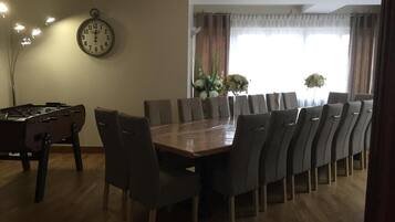 A dining area with a long table, chairs, a clock, and a window with curtains.