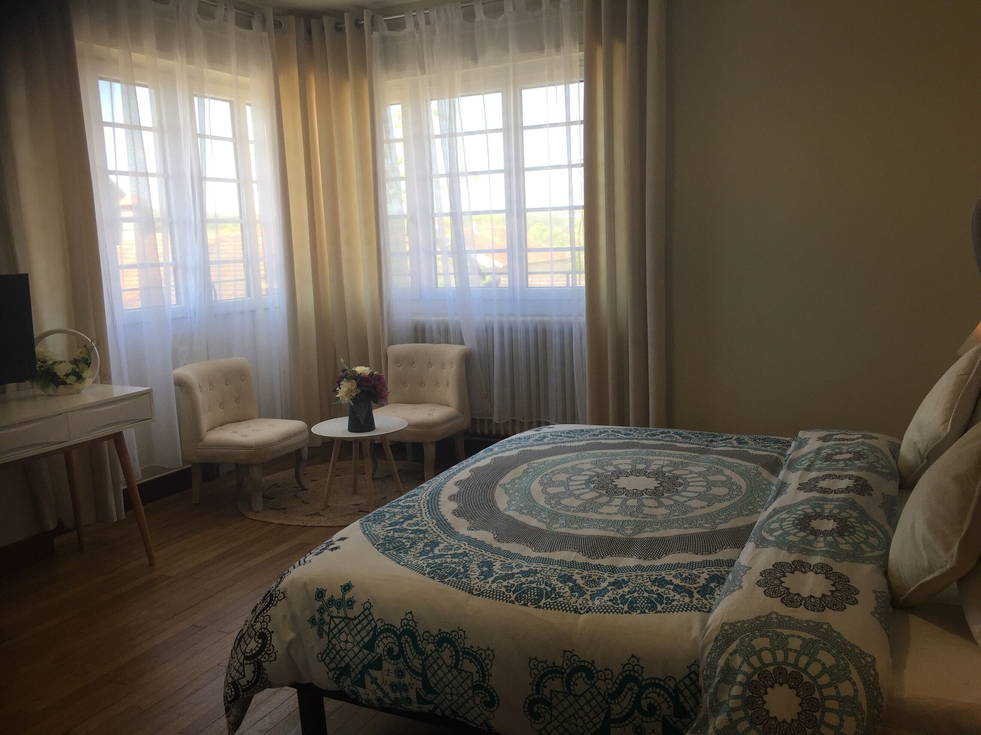A bedroom with a large bed, two chairs, a small table with a vase, and a desk with a computer.