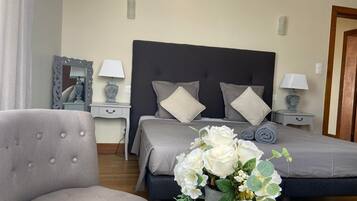 Une chambre d’hôtel avec un lit, une chaise, une table de chevet avec une lampe, un miroir et un vase avec des fleurs.