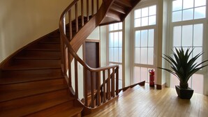 A wooden staircase leading to a landing with large windows and a potted plant.