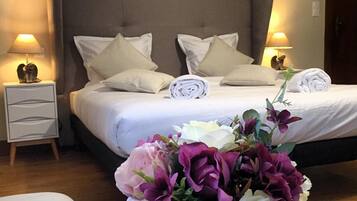 A hotel room with a bed, pillows, a nightstand, a lamp, a cat figurine, and a flower arrangement.