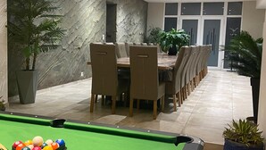 A dining area with a pool table, chairs, and potted plants.