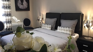 A bedroom with a bed, bedside tables, a chair, a wall-mounted artwork, and a window with curtains.