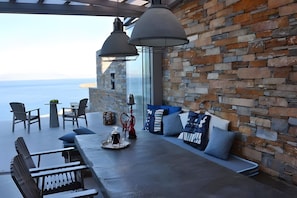 A modern outdoor seating area with stone walls, a long table, and two hanging lights. - Villa 'Lina Syros' with Sea View, Wi-Fi and Air Conditioning (Syros)