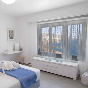 A bedroom with a bed, a bedside table, a window with a view, and a small shelf with decorative items. - Villa 'Lina Syros' with Sea View, Wi-Fi and Air Conditioning (Syros)