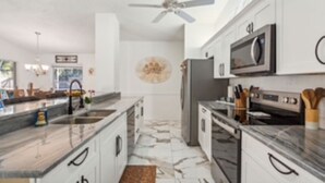 A modern kitchen with white cabinets, a marble countertop, a built-in microwave, and a ceiling fan. - Renovated 4BR Sarasota Home Private Heated Pool 28-Day Min Near Siesta Key (Sarasota)