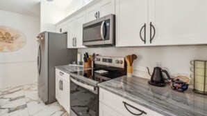 A modern kitchen with white cabinets, a stainless steel refrigerator, a microwave, and a gas stove. - Renovated 4BR Sarasota Home Private Heated Pool 28-Day Min Near Siesta Key (Sarasota)