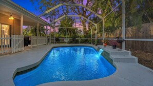 A swimming pool with a curved edge, surrounded by a covered patio area with chairs and potted plants. - Renovated 4BR Sarasota Home Private Heated Pool 28-Day Min Near Siesta Key (Sarasota)