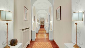 A long hallway with white columns, framed pictures, and floor lamps.