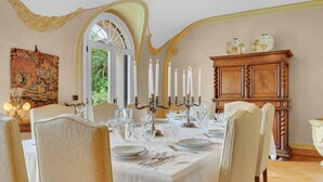 A dining room with a table set for four, a wooden cabinet, and a tapestry on the wall.