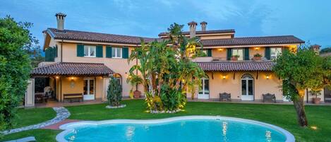 A large house with a swimming pool, green lawns, and outdoor seating.