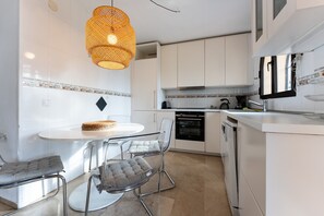 Een moderne keuken met witte kasten, een ronde eettafel, twee stoelen en een hanglamp.